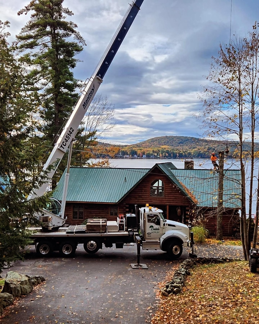 A crane being used to provide tree services in front of a log cabin.